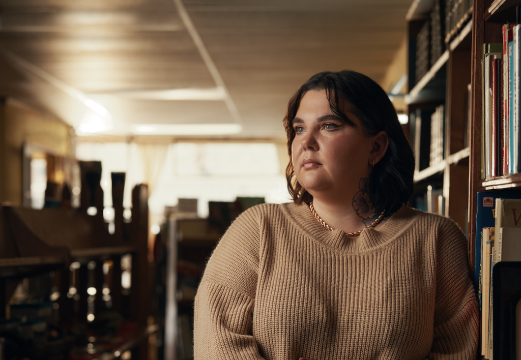 Woman leaning against a bookshelf, looking off in the distance
